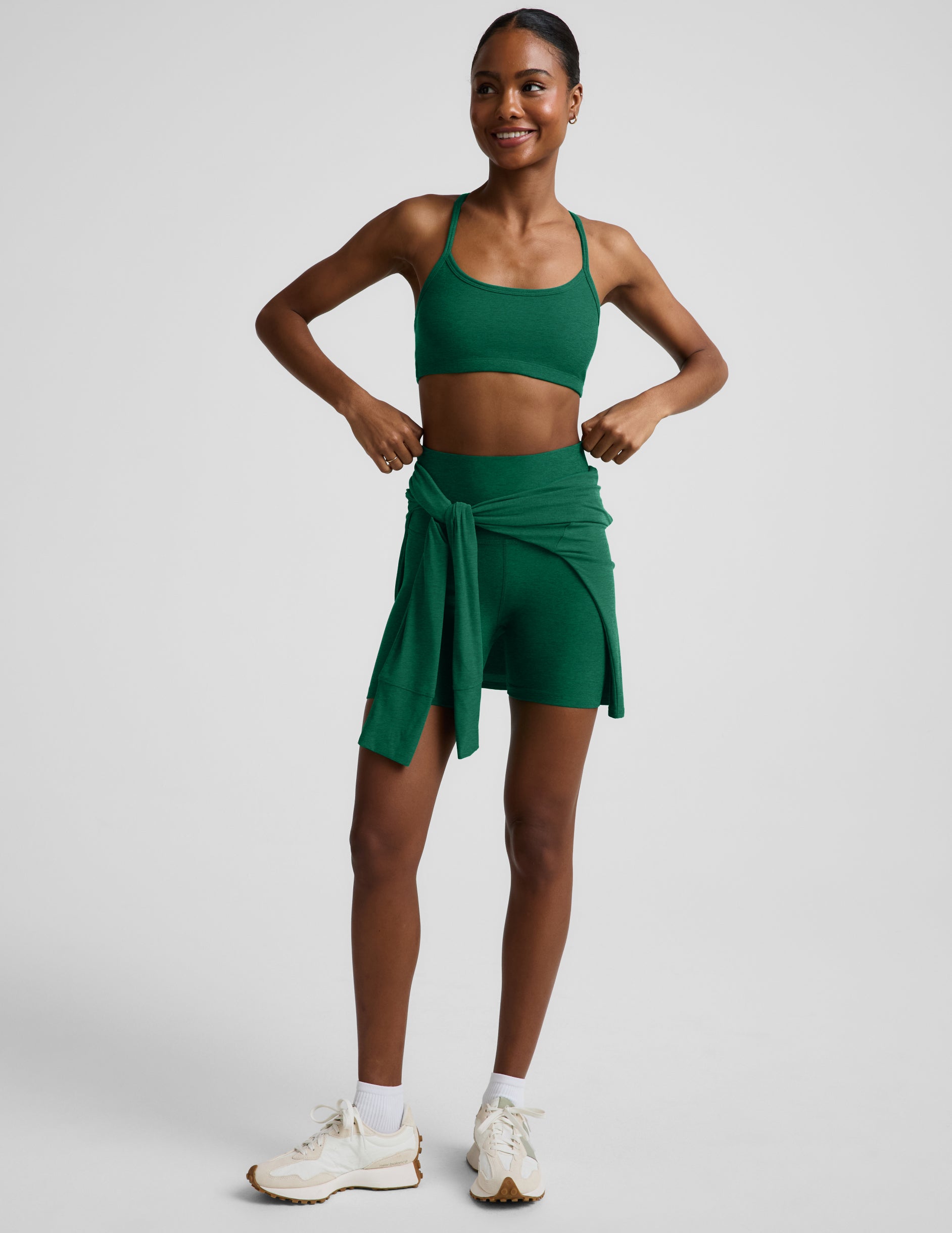 Woman wearing a green racerback bra and 5" biker shorts against a plain background.