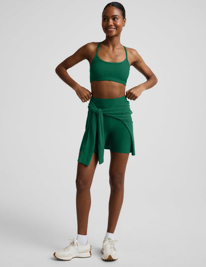 Woman wearing a green racerback bra and 5" biker shorts against a plain background.