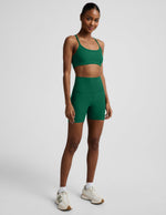 Woman wearing a green racerback bra and 5" biker shorts against a plain background.