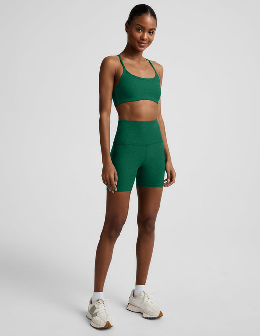 Woman wearing a green racerback bra and 5" biker shorts against a plain background.
