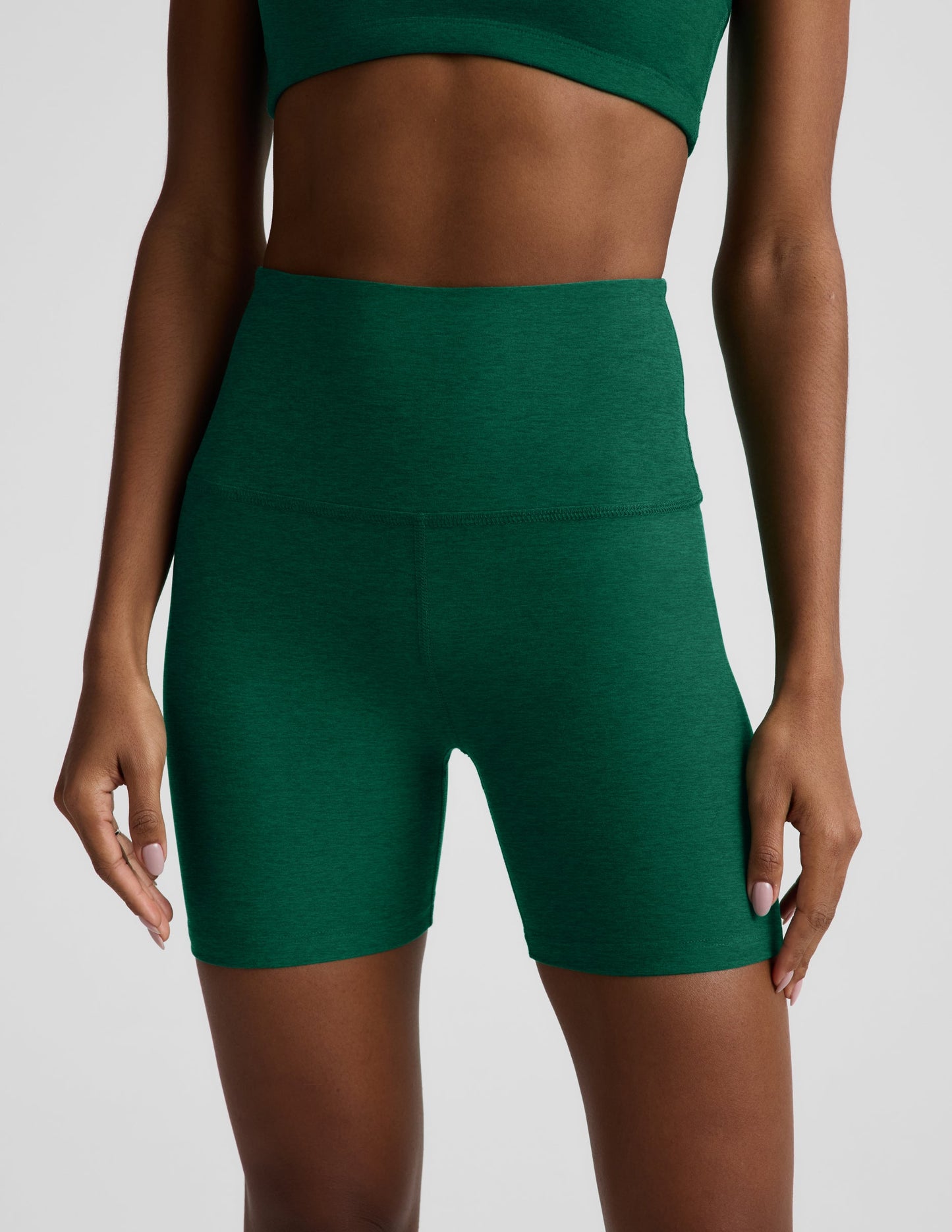 Woman wearing a green racerback bra and 5" biker shorts against a plain background.