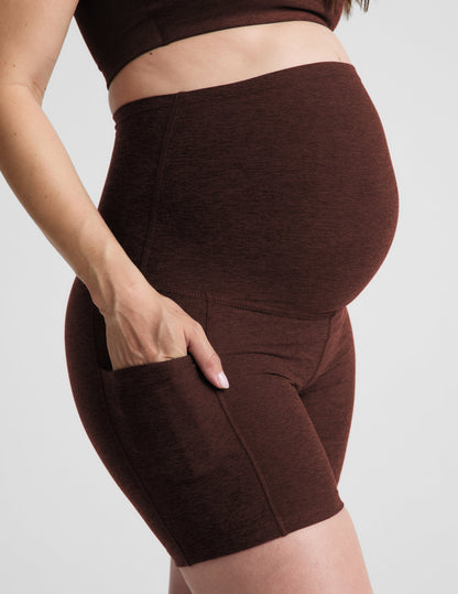 Woman wearing Brown Spacedye™ Keep Pace 5" Maternity Pocket Biker Short paired with a matching sports bra, side profile.