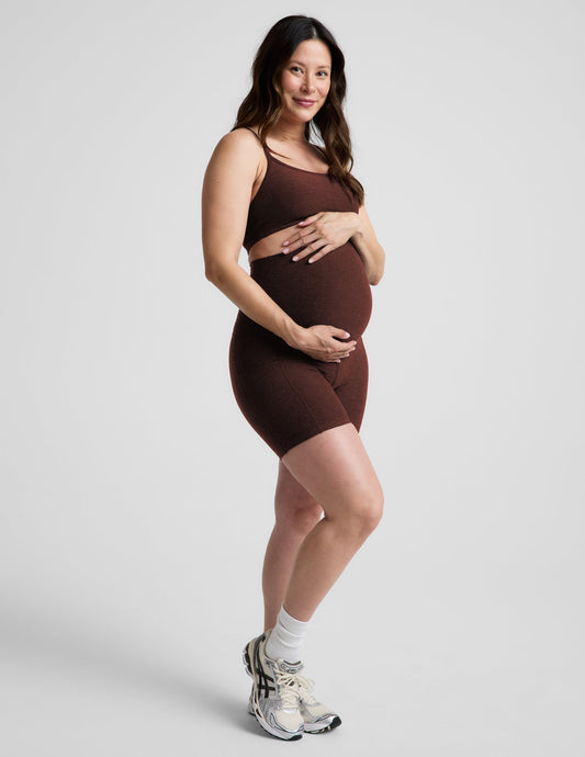 Woman wearing Brown Spacedye™ Keep Pace 5" Maternity Pocket Biker Short, paired with a matching bra. Side profile.