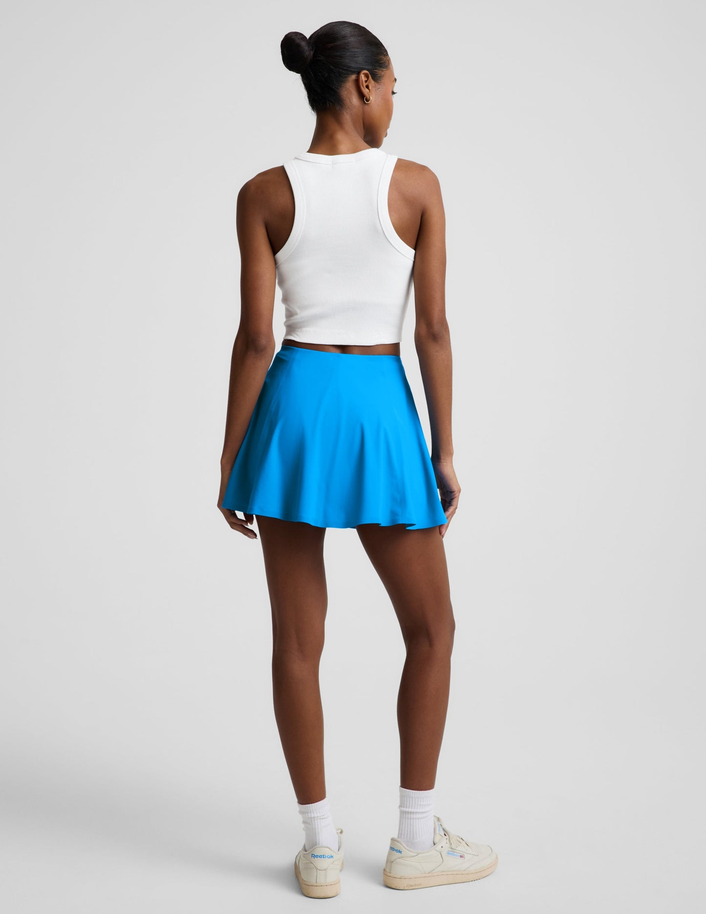Rear view of woman wearing Blue You're A Force™ Skirt paired with a white tank top and cream sneakers.