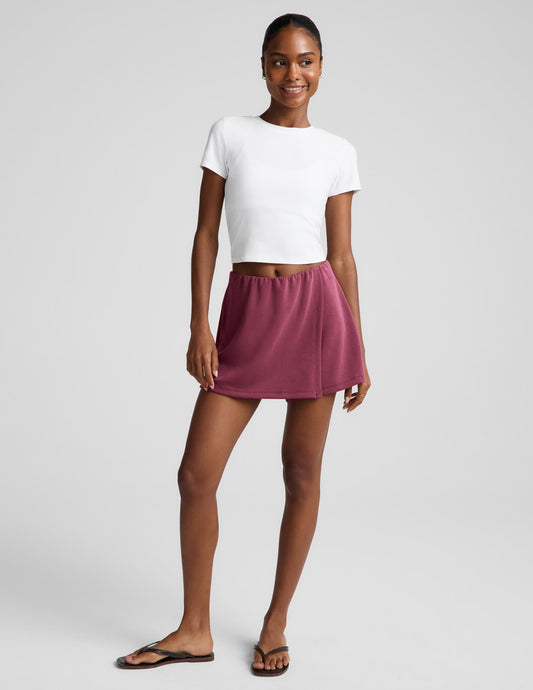 Woman wearing a white t-shirt and mauve skort against a plain background.