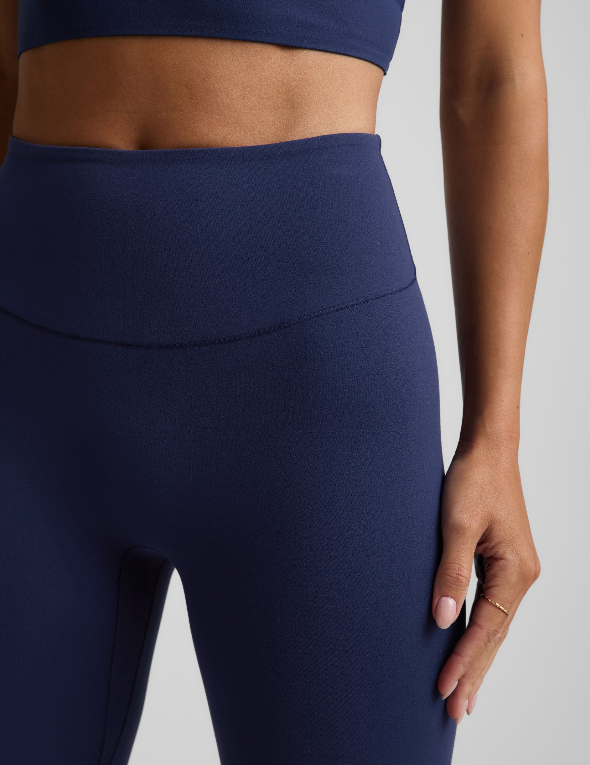 Woman wearing a blue cropped tank and blue midi leggings against a plain background.