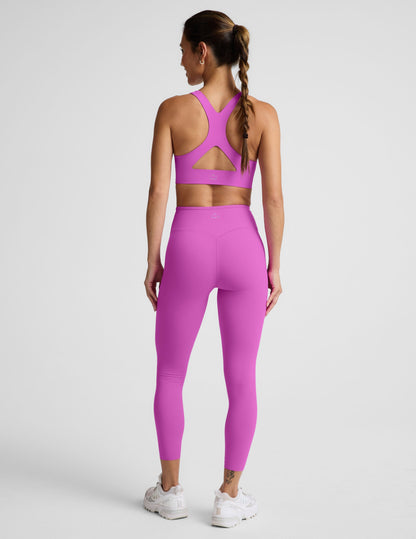 Woman wearing a purple sports bra and purple midi length leggings against a plain background.