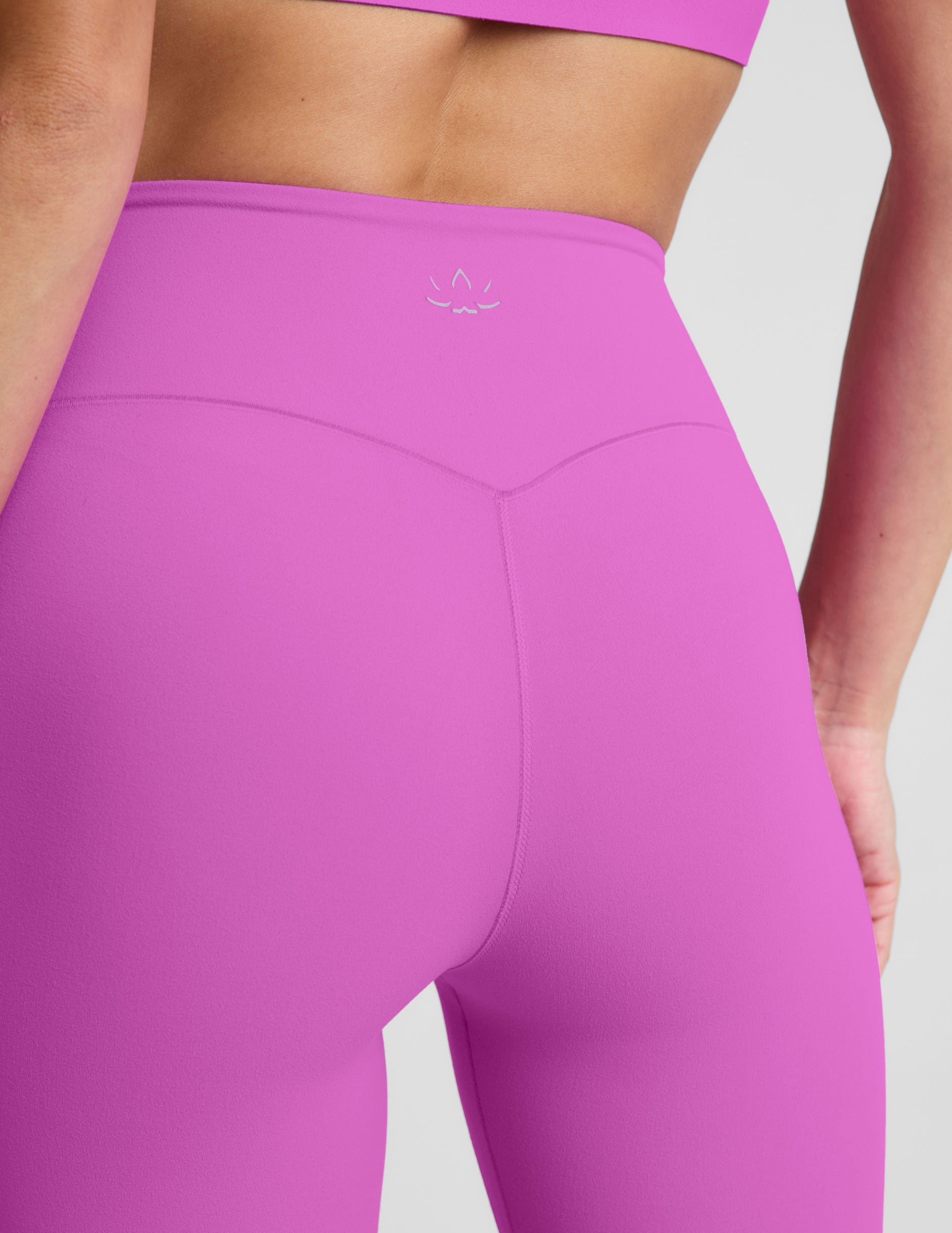 Woman wearing a purple sports bra and purple midi length leggings against a plain background.