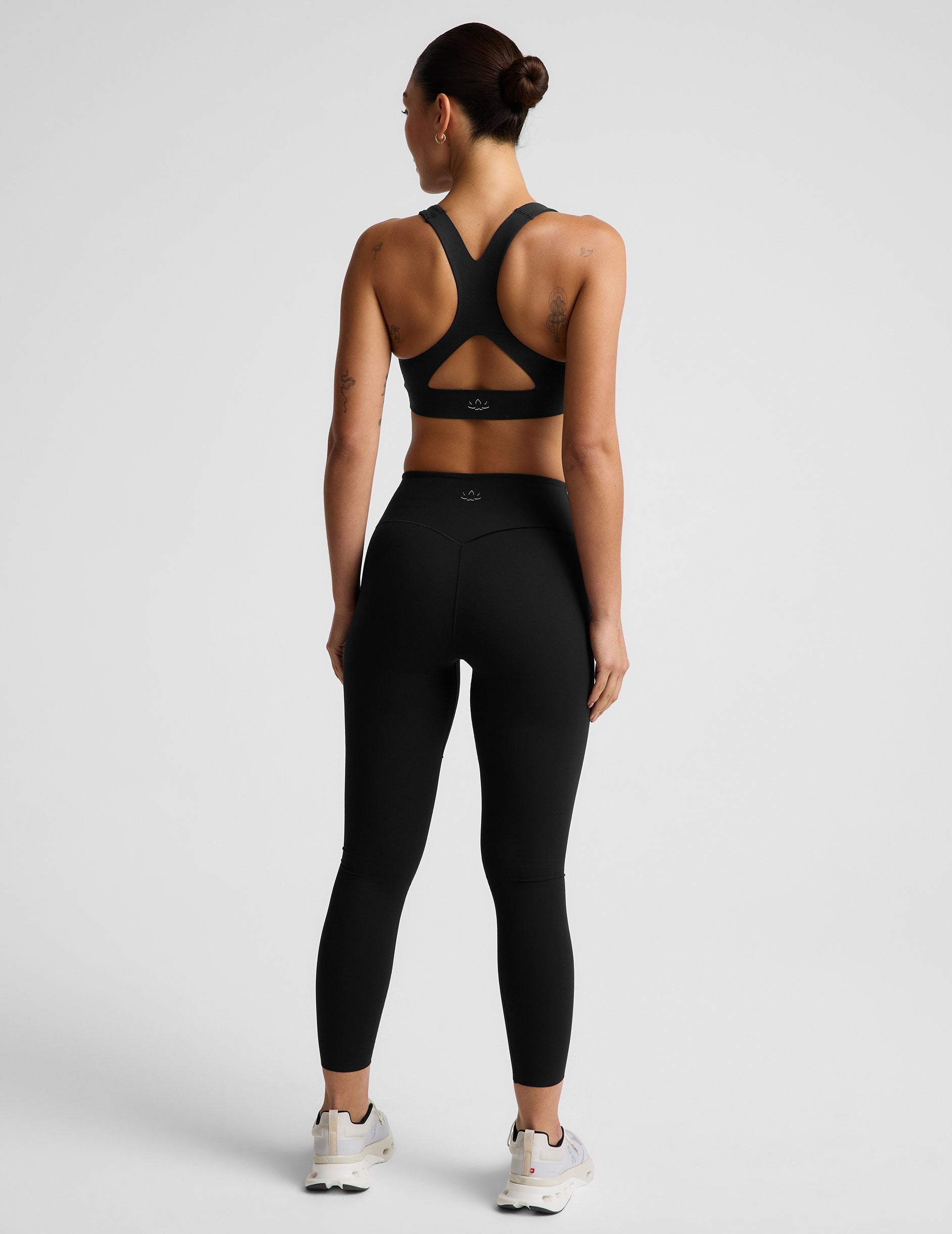 Woman wearing a black sports bra and black midi length leggings against a plain background.