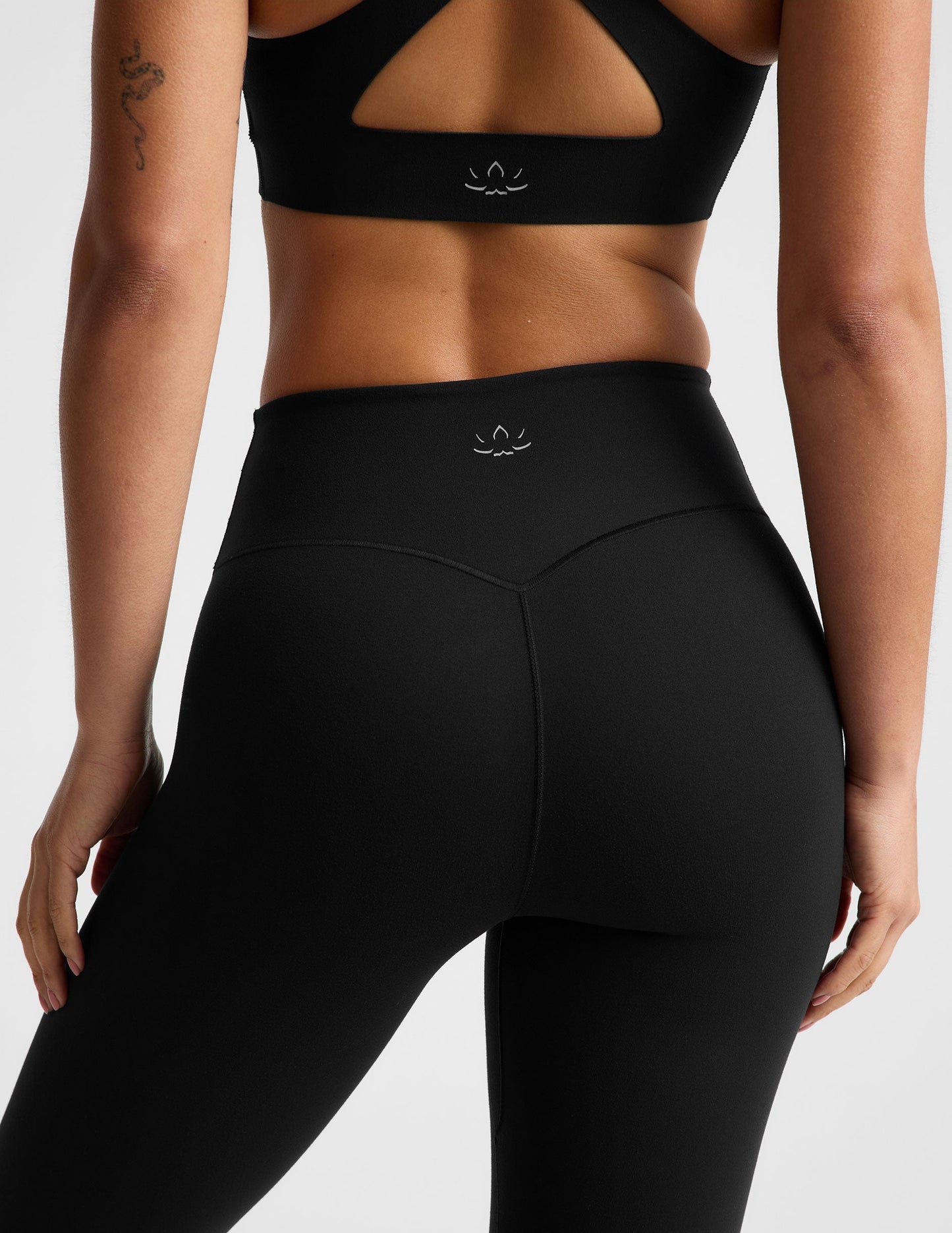 Woman wearing a black sports bra and black midi length leggings against a plain background.