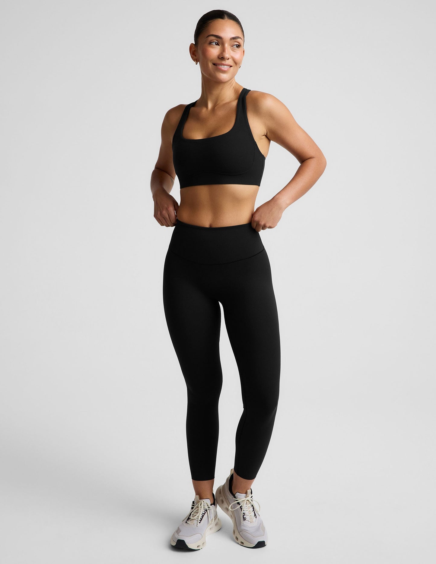 Woman wearing a black sports bra and black midi length leggings against a plain background.