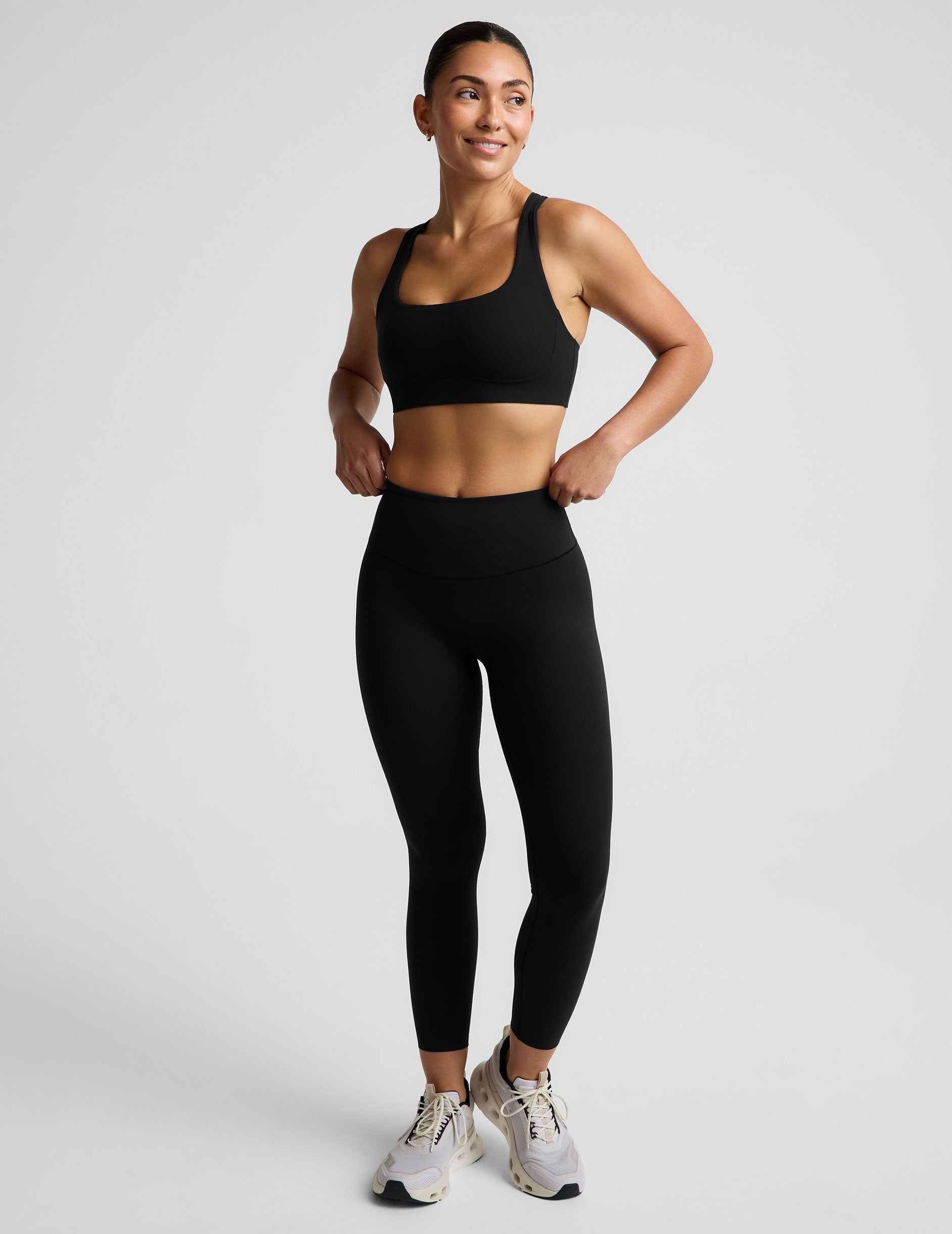 Woman wearing a black sports bra and black midi length leggings against a plain background.