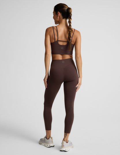 Woman wearing a brown cropped tank and brown midi length leggings against a plain studio background.