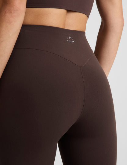 Woman wearing a brown cropped tank and brown midi length leggings against a plain studio background.