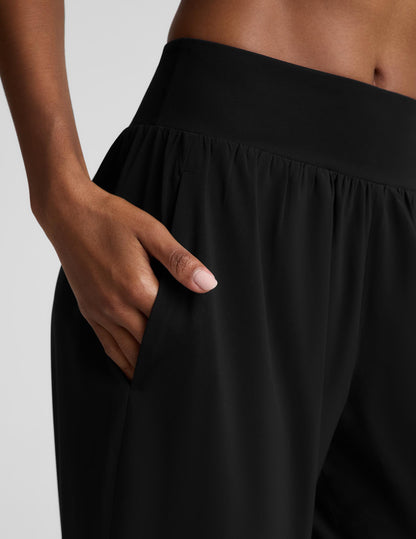 A woman modeling a black two-piece activewear set consisting of a bra and high-waisted wide-leg pants, photographed against a solid light gray studio background.