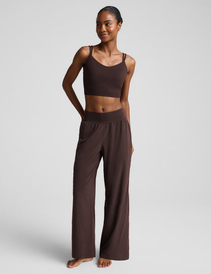 A woman modeling a matching dark brown lounge set consisting of a cropped tank top and wide-leg pants, photographed against a neutral light gray studio background.