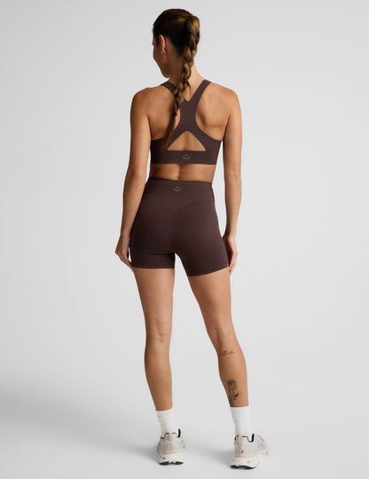 Woman wearing a brown sports bra and brown biker shorts against a plain background.