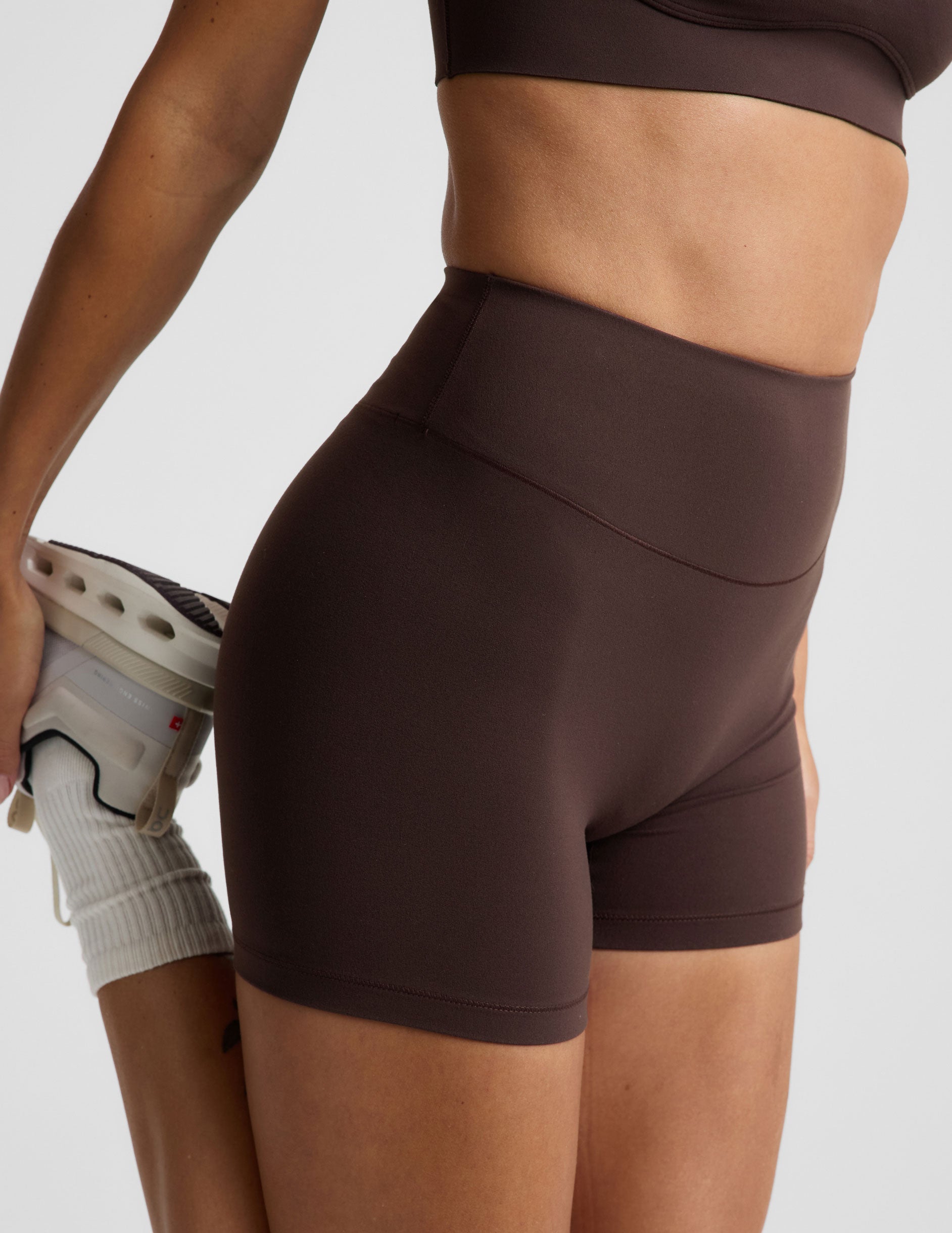 Woman wearing a brown sports bra and brown biker shorts against a plain background.