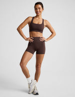 Woman wearing a brown sports bra and brown biker shorts against a plain background.