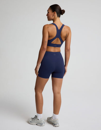 Woman wearing a blue sports bra and blue biker shorts against a plain background.