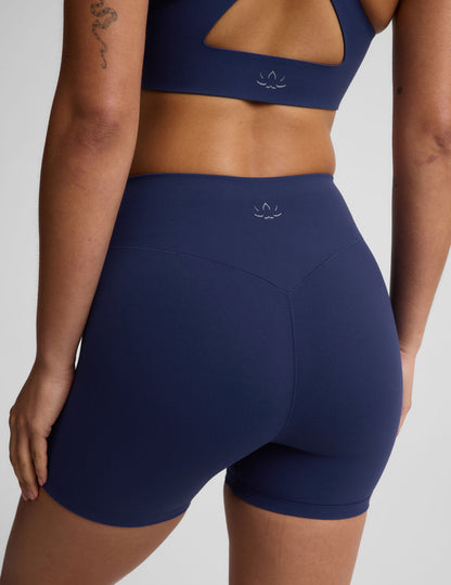 Woman wearing a blue sports bra and blue biker shorts against a plain background.