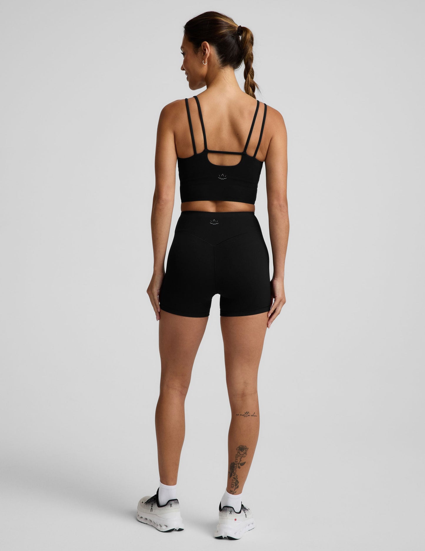 Woman wearing a black cropped tank and black biker shorts against a plain background.