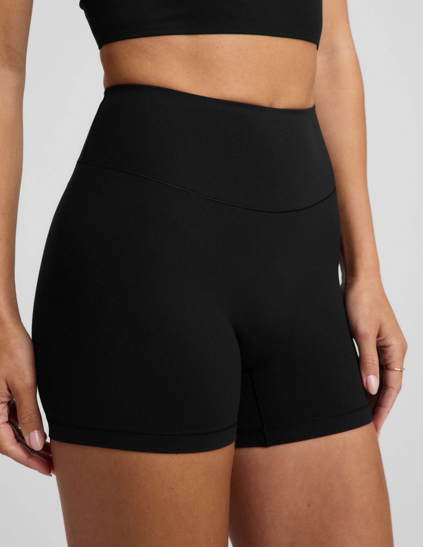 Woman wearing a black cropped tank and black biker shorts against a plain background.