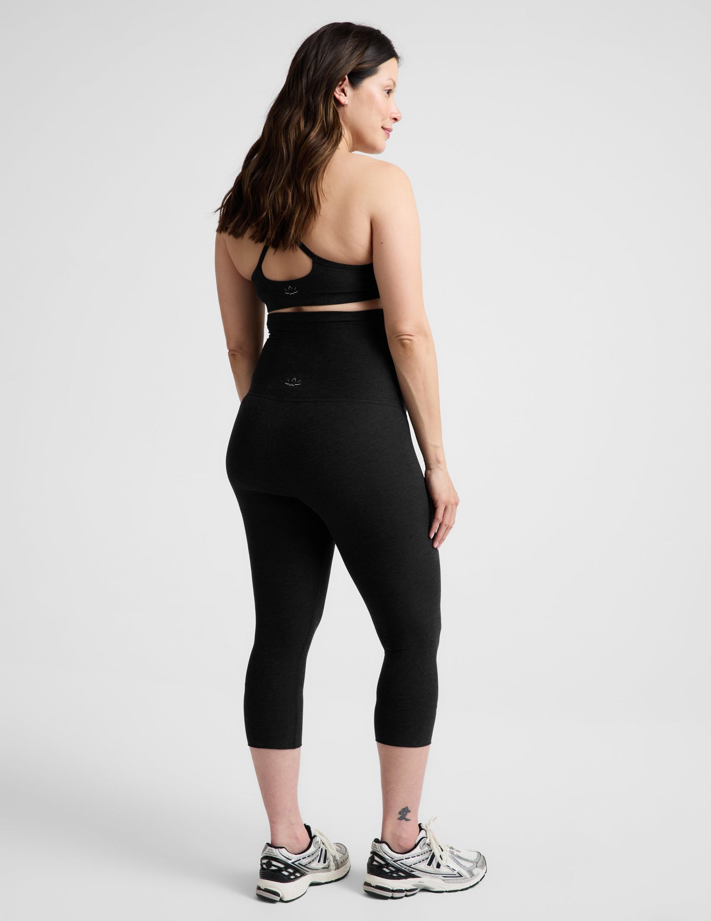 Rear view of woman wearing Black Spacedye™ Love The Bump Maternity 20.5" Capri Legging with a sports bra and sneakers.