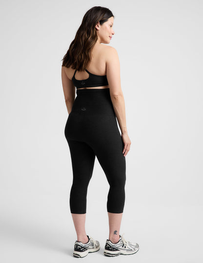 Rear view of woman wearing Black Spacedye™ Love The Bump Maternity 20.5" Capri Legging with a sports bra and sneakers.