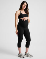 Woman wearing Black Spacedye™ Love The Bump Maternity 20.5" Capri Legging paired with a black sports bra and sneakers.