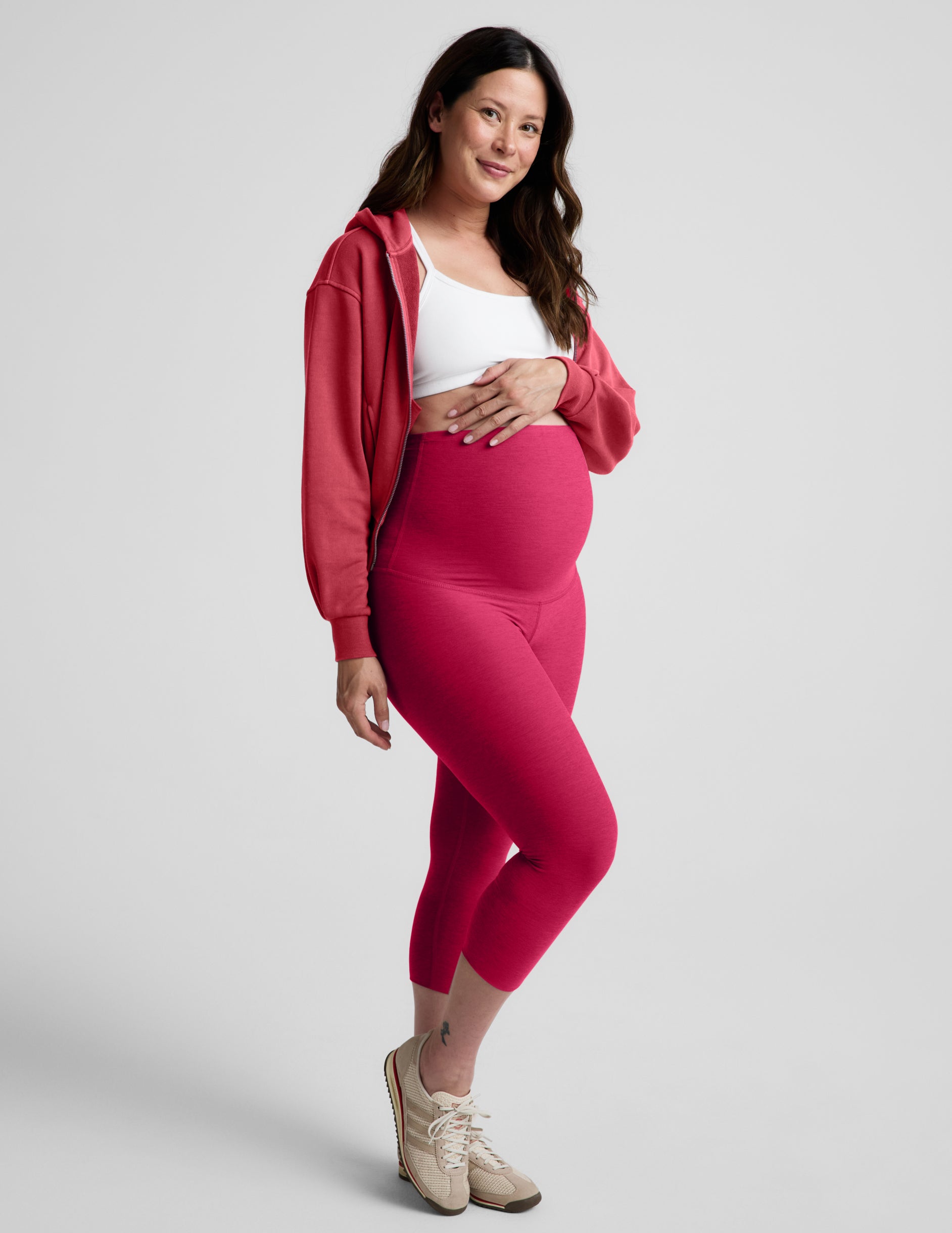 Woman wearing Pink Spacedye™ Love The Bump Maternity 20.5" Capri Legging paired with a pink zip-up hoodie and white sports bra.