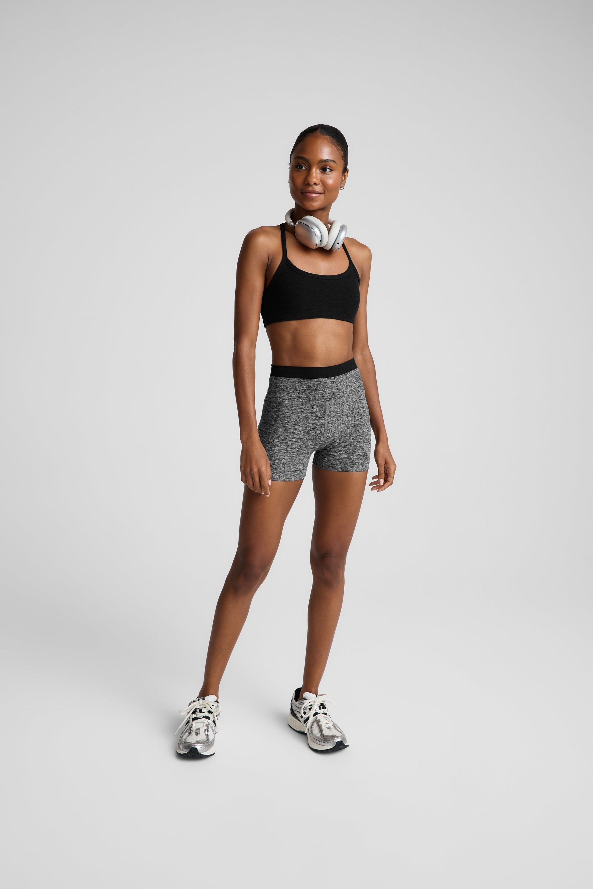 Woman wearing a black bra and heather gray biker shorts against a plain background.