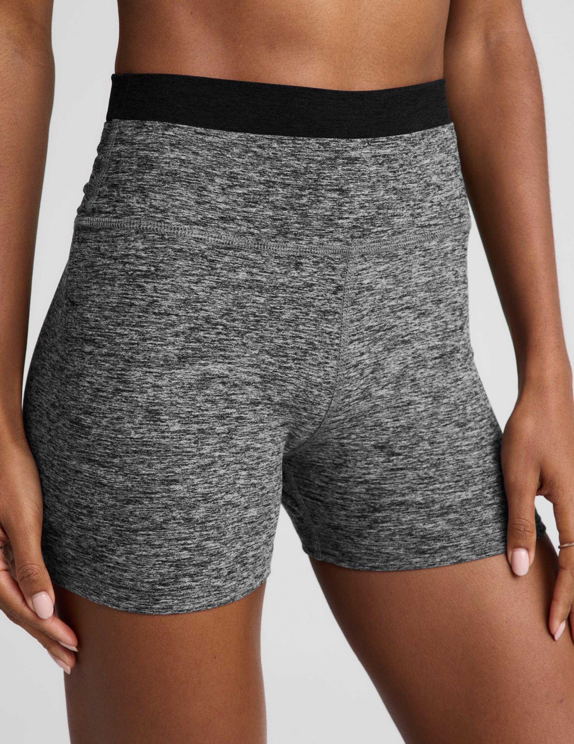 Woman wearing a black bra and heather gray biker shorts against a plain background.