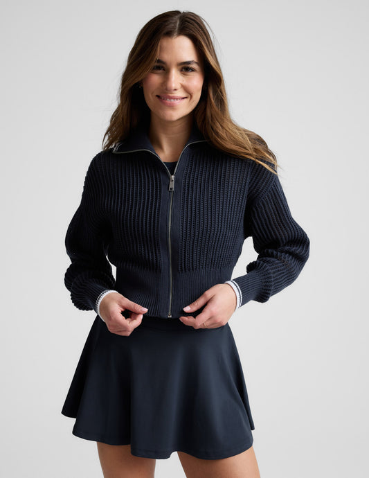 Woman wearing a blue zip-up sweater and skirt against a plain background.