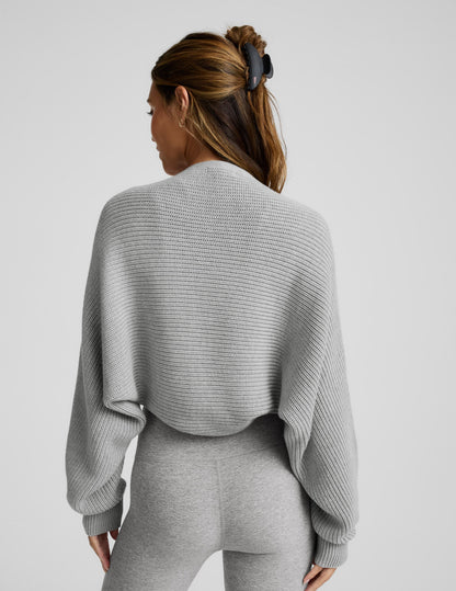 Woman wearing a gray shrug on a light gray background.