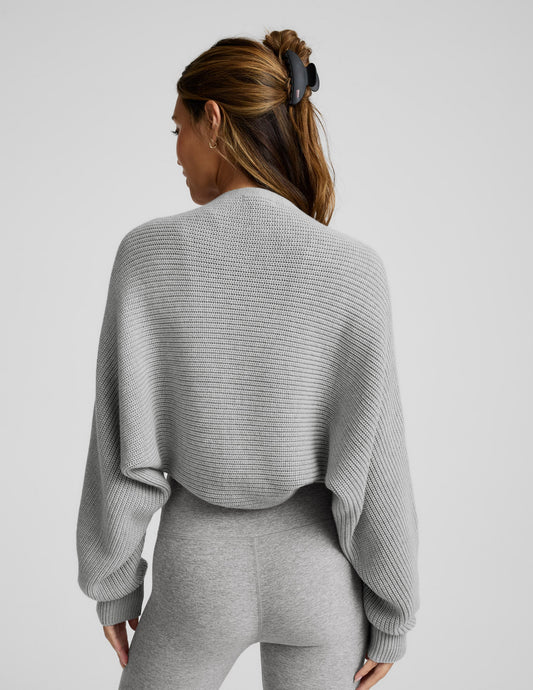 Woman wearing a gray shrug on a light gray background.