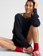 Woman wearing a navy sweater and red sneakers sitting on a light gray background.