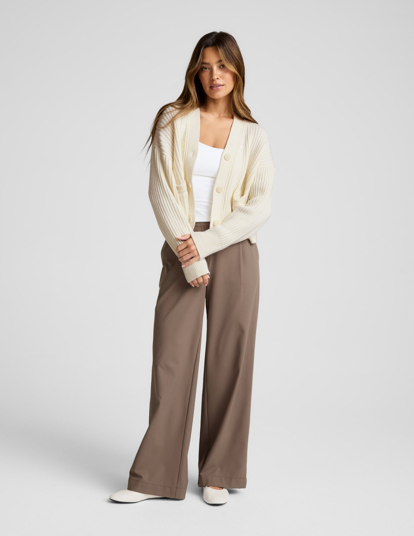 woman wearing a cream cardigan on a plain background.
