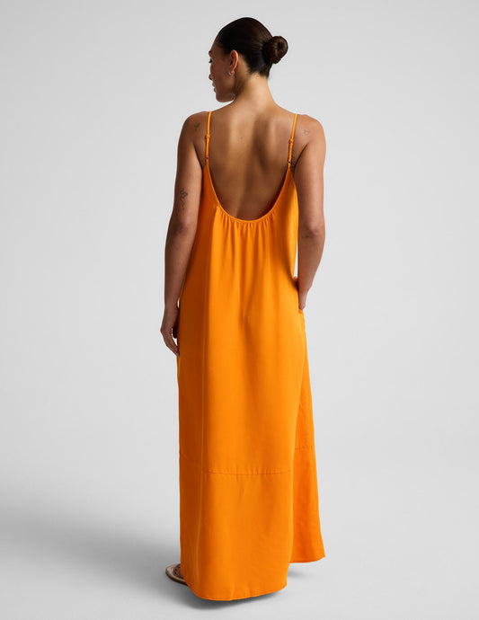 Woman wearing an orange maxi cupro dress against a plain background.