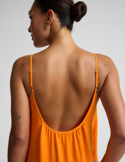 Woman wearing an orange maxi cupro dress against a plain background.