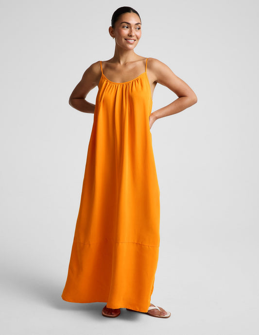 Woman wearing an orange maxi cupro dress against a plain background.