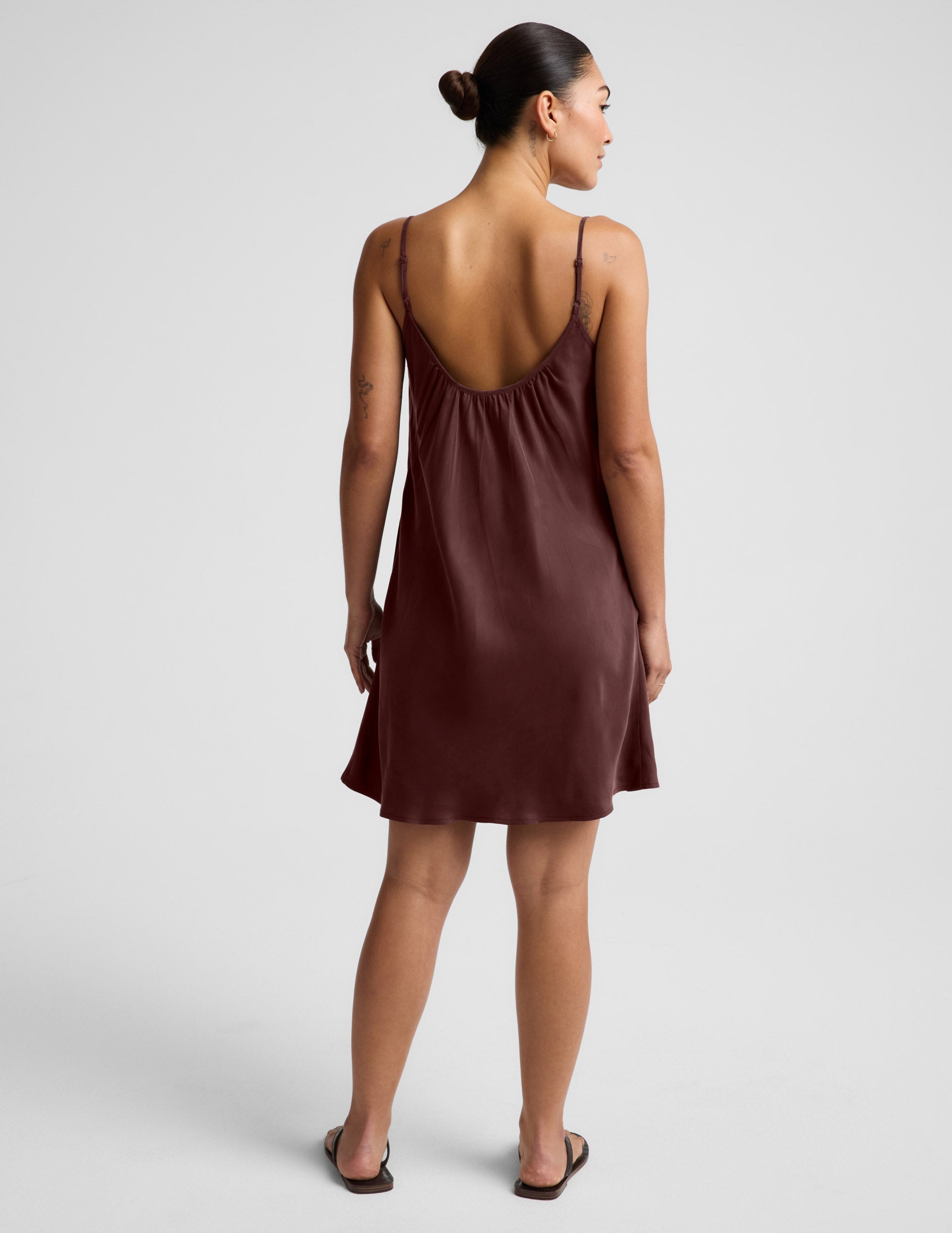 Woman wearing a brown cupro mini dress and black sandals against a plain background.