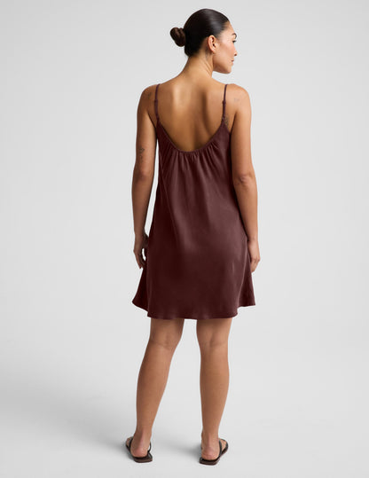 Woman wearing a brown cupro mini dress and black sandals against a plain background.