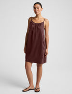 Woman wearing a brown cupro mini dress and black sandals against a plain background.