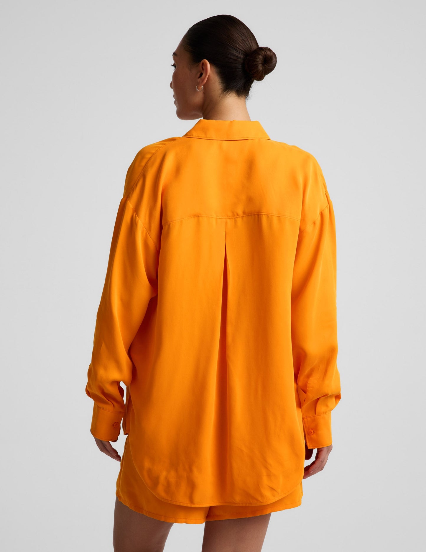 Woman wearing an orange button down shirt and orange shorts against a plain background.