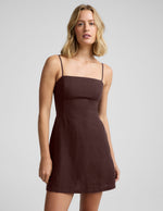 Woman wearing a brown mini linen dress against a plain background.