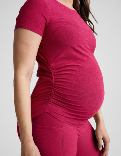 Pregnant woman wearing a red maternity t-shirt and shorts against a plain background.