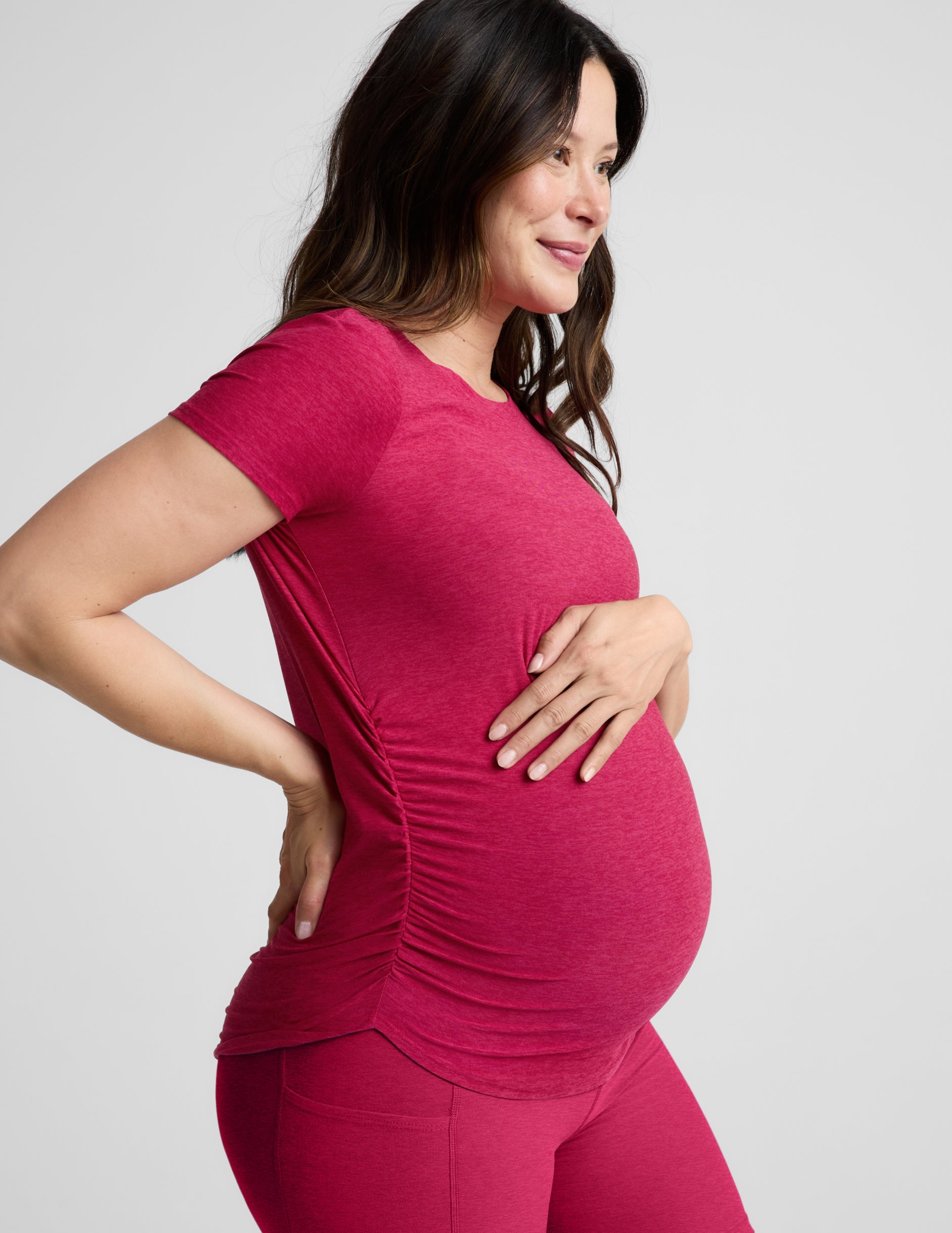 Pregnant woman wearing a red maternity t-shirt and shorts against a plain background.