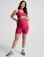 Woman wearing a red maternity tank top and biker shorts against a plain background.