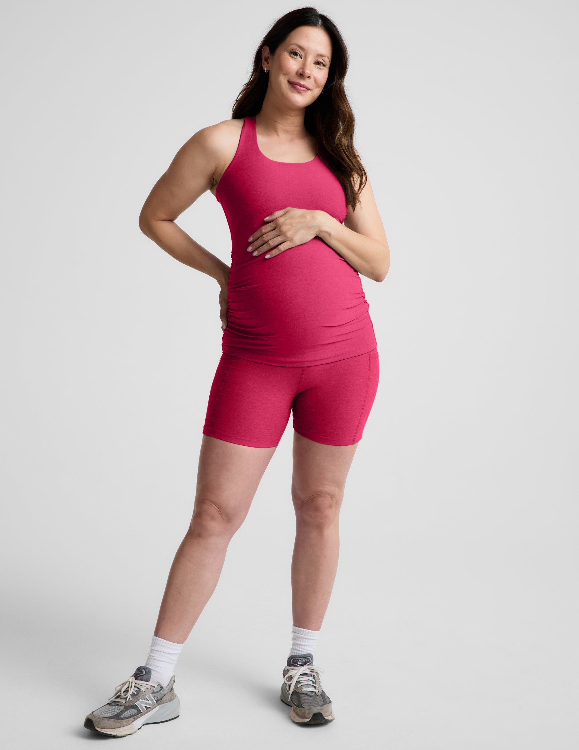 Woman wearing a red maternity tank top and biker shorts against a plain background.